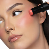 Applying MINË Plumping Blush Stick in Peach Melt to the cheek